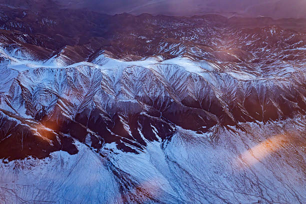 Watching the texture of snow capped mountains from a plane at dusk