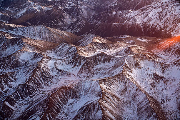 Watching the texture of snow capped mountains from a plane at dusk