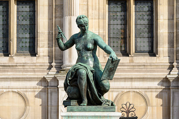 Bronze sculpture of a seated female figure holding a compass and tablet, displayed in front of the historic stone facade and tall windows of Hotel de Ville in Paris, illuminated by natural daylight.