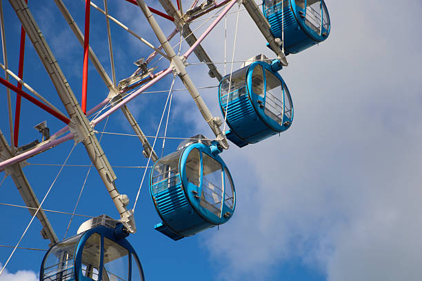 Colorful Ferris wheel gondolas against bright blue sky and clouds.