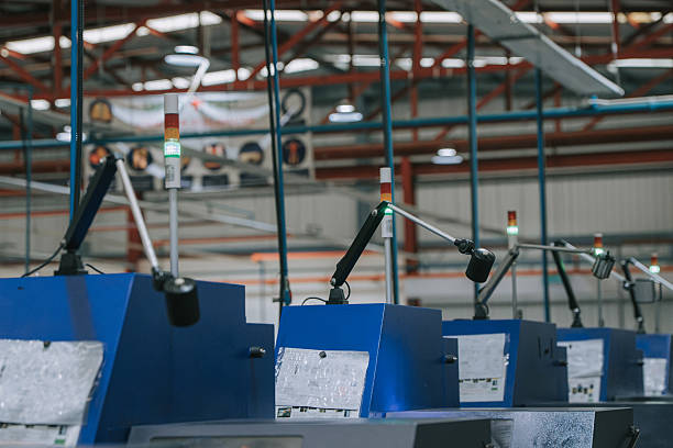 Row of industrial automation machines with task lighting and indicator lights inside a modern manufacturing facility, emphasizing production technology and factory operations