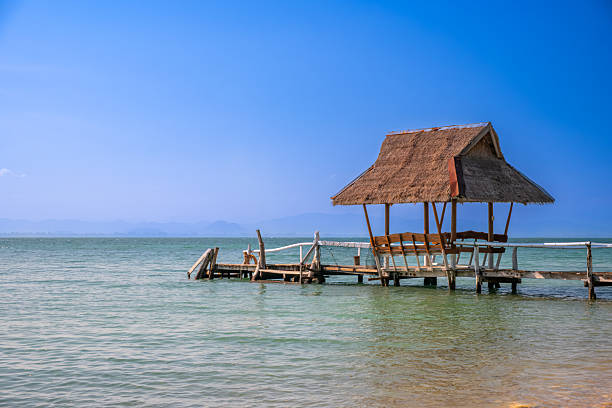 Tropical escape, rustic pier hut over turquoise sea under clear blue sky—perfect for travel ads, beach screensavers, or serene vacation backgrounds.