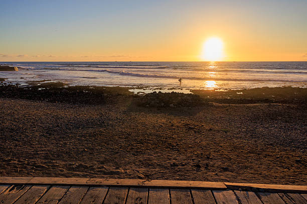 Sundown over Atlantic Ocean panorama with surfer carrying a surfboard at a beach in holiday resort Playa de las Americas on Canary Island Tenerife, Spain