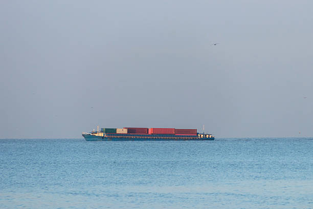 A container ship carrying stacked cargo containers on calm sea at sunrise with serene sky