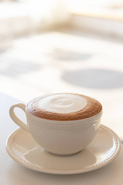 Creamy cappuccino in white ceramic cup on saucer with soft morning light and cozy atmosphere
