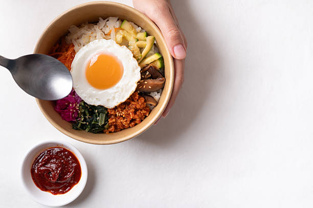 Bibimbap, Korean food, Cooked rice with vegetables, pork and egg in a bowl with hand