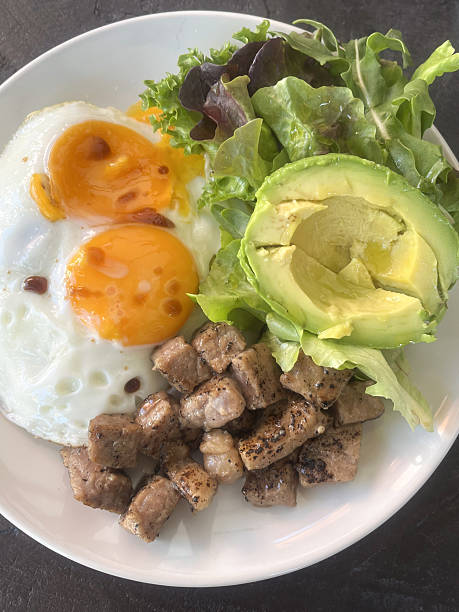Sunny fried egg yolk avocado salad with grilled pork cubes and green lettuce, fresh and appetizing morning meal