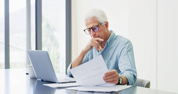 istock Laptop, thinking and old man with documents, financial analysis and bills with retirement fund. Pc, home and senior person with paperwork, debt and asset management with insurance policy and decision 2255021918