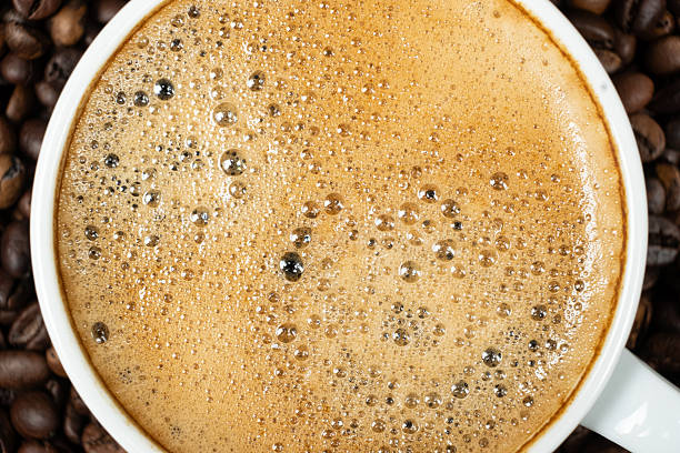Top view of a white cup filled with fresh espresso on a coffee bean background
