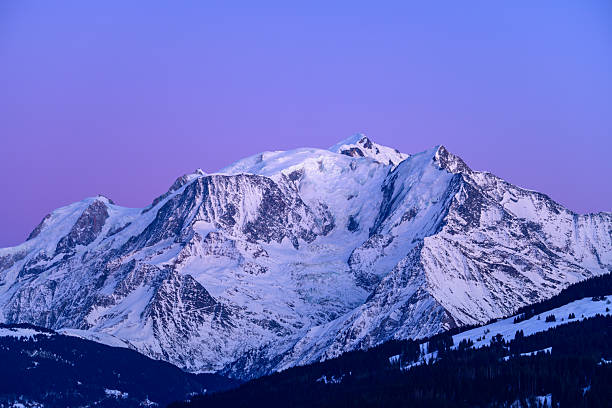 The snow-covered Mont Blanc massif stands out against a vivid violet twilight sky, with crisp glacier textures and dark forested slopes in the foreground.