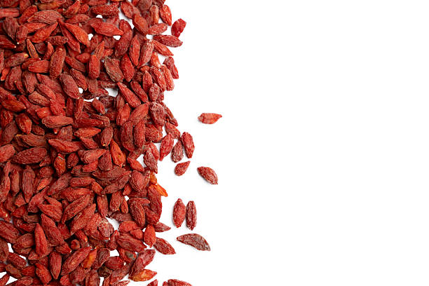 A pile of dried goji berries scattered on the left side of a white background. The bright red color and wrinkled texture highlight their natural, nutrient-rich qualities. Commonly used in healthy snacks, teas, and superfood blends.