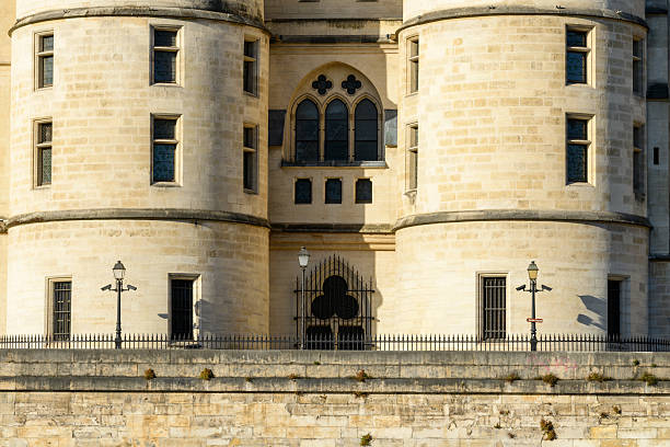 Close-up of two rounded stone towers with narrow windows and ornate arched details, illuminated by golden afternoon light at La Conciergerie in Paris.