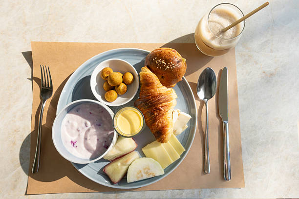 Assorted baked goods on a white plate including cake, Bakery set, Round Bun, and mini croissant with a gold spoon and pink cup, ideal for food photography and menu use, Top view