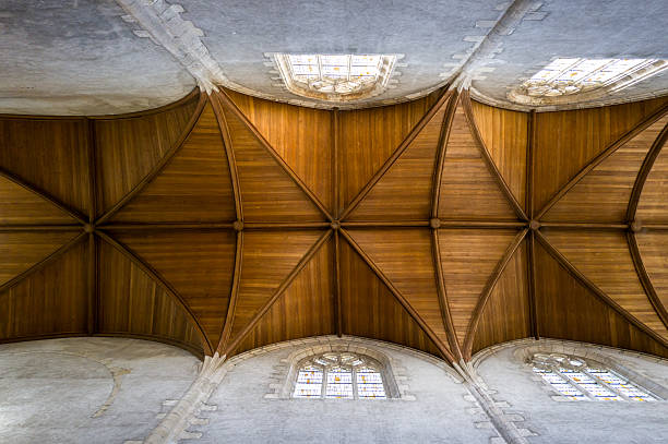 Symmetrical ribbed wooden vault ceiling with pointed arches and stone window frames in a historic church at Chateauneuf-sur-Loire. Natural light highlights the warm wood tones and geometric design.