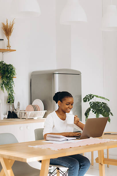 istock Young black woman telecommuting from home kitchen, working on laptop computer and drinking coffee 2255041734
