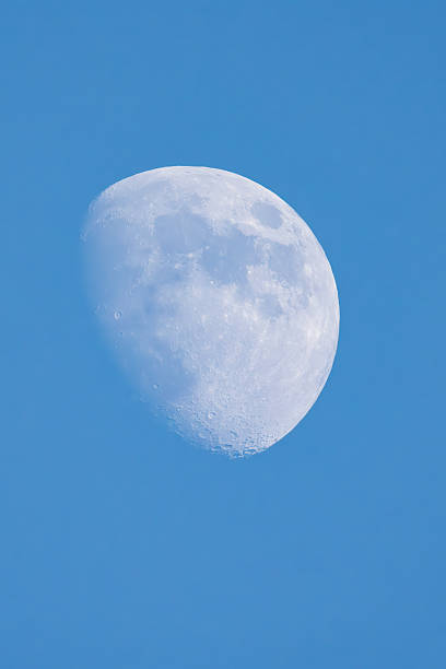A detailed view of a thin crescent moon in its waxing phase, positioned against a blue daytime sky, capturing the subtle glow and craters on the lunar surface. The image emphasizes the serene contrast between the pale moon and the expansive sky, evoking a sense of cosmic tranquility. No people are present, focusing solely on the celestial body and atmospheric setting. Ideal for commercial uses in astronomy publications, educational materials on lunar phases, space exploration articles, night sky calendars, and backgrounds for science fiction media or environmental awareness campaigns highlighting natural wonders.