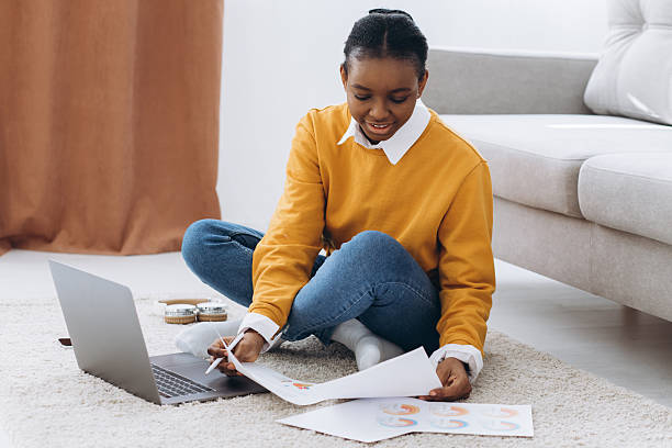 istock Young woman analyzing business data and financial documents while sitting on the floor at home, using a laptop for remote work 2255042927