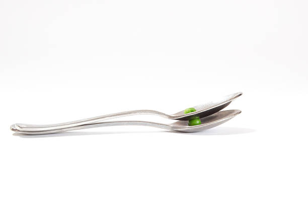 Two table spoons on top of each other with a green pea each