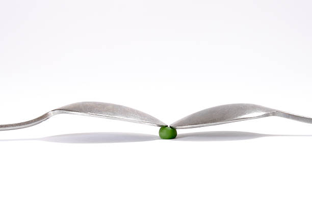A green pea squeezed by the tips of two table spoons