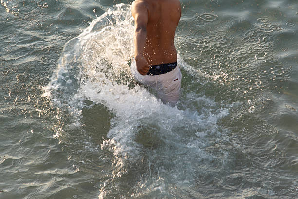 Salvador, Bahia, Brazil - January 3, 2026: Close-up of a man entering and running in the sea, creating splashes of water under the daylight in Salvador, Bahia.