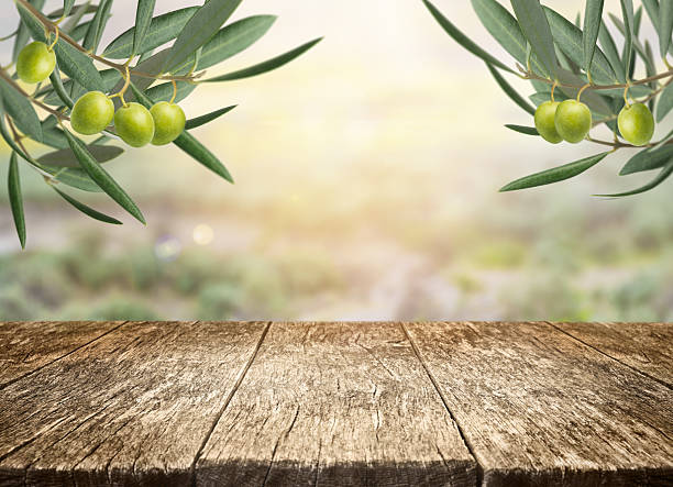 istock Fresh olive branch and rustic wooden table with copy space for product display over blurred landscape background. 2255046876