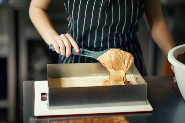 Closeup of unrecognizable women putting cake batter into multiple baking trays.