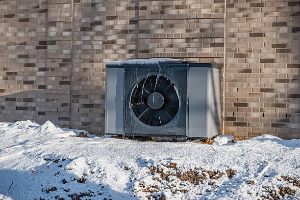 istock Air source heat pump unit with icicles hanging from casing installed against modern brick building surrounded by snow during winter. Energy-efficient residential heating technology. 2255048157