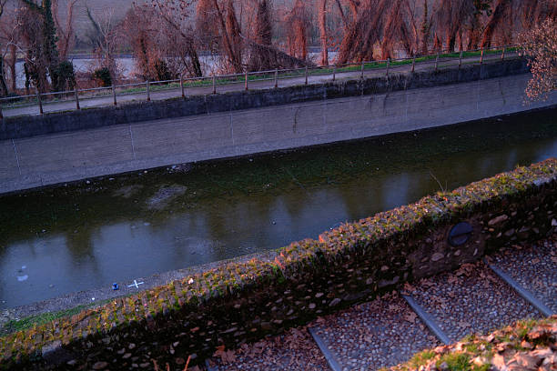 Sunset over a river landscape in Tornavento, northern Italy. The low sun casts warm light across the horizon, silhouetting trees and surrounding countryside, while reflections appear on the calm water below. The scene conveys tranquility, transition, and the peaceful atmosphere of the Italian landscape at dusk.