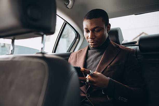 istock Young smiling african man using smartphone while sitting on backseat in car. Concept of happy business people traveling. 2255050577