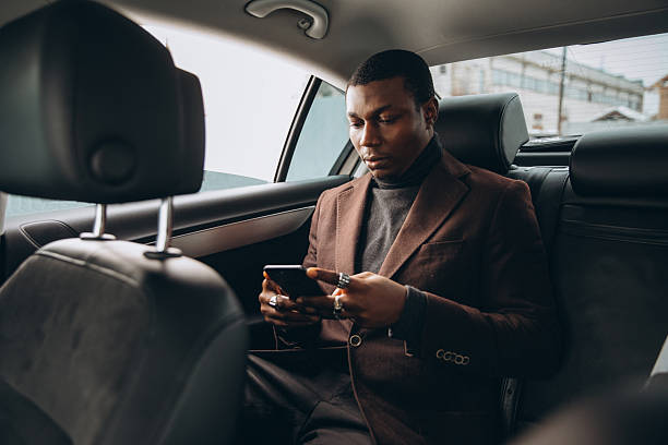 istock Young smiling african man using smartphone while sitting on backseat in car. Concept of happy business people traveling. 2255050593