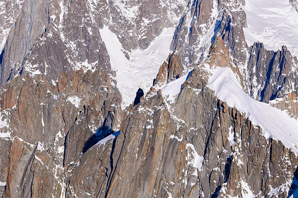 Sharp granite spires and rugged cliffs rise from the Mont Blanc massif, their jagged forms dusted with snow and illuminated by crisp winter sunlight.