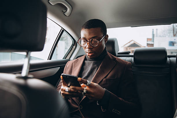 istock Young smiling african man using smartphone while sitting on backseat in car. Concept of happy business people traveling. 2255051668