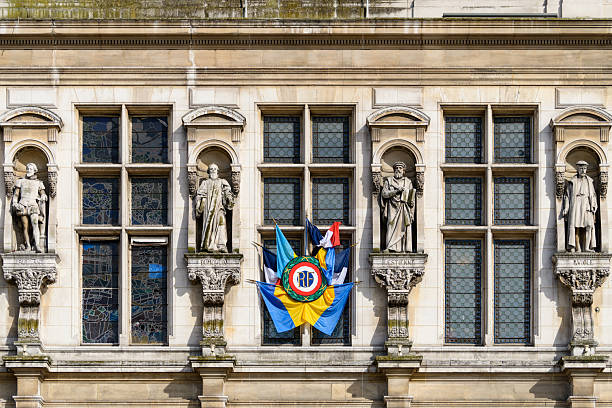 Row of classical stone statues and stained glass windows on the ornate facade of Hotel de Ville in Paris, with vibrant flags and bright daylight enhancing architectural details.