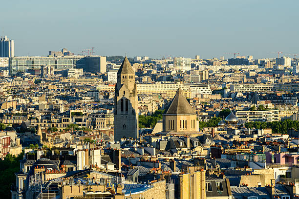 Elevated view of Saint-Pierre-de-Chaillot church with its distinctive tower and dome rising over classic Parisian rooftops, set against a sprawling urban skyline in warm afternoon light.