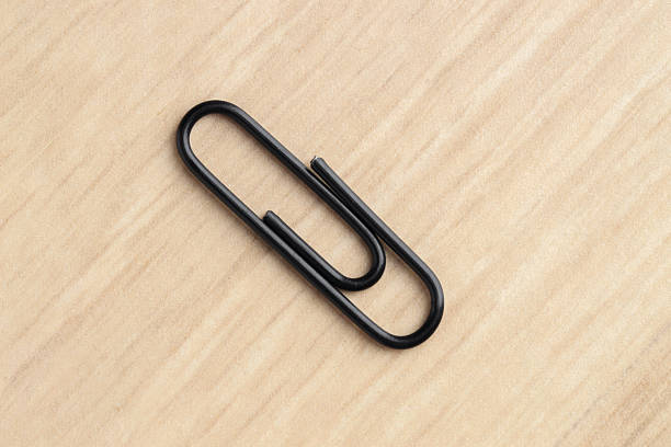 One black paper clip on wooden table, top view