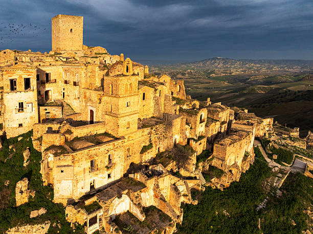 Dramatic view of the abandoned village of Craco at sunset, Matera province, Basilicata, South of Italy, Italy, EuropeCraco is an evocative abandoned village in southern Italy, situated in the Basilicata region near Matera. Perched dramatically on a hill, it is renowned for its striking, desolate atmosphere and strong sense of history. Founded in the early Middle Ages, the settlement is characterized by winding alleys, ancient stone buildings, and panoramic views over the surrounding countryside.The village was gradually deserted due to severe soil erosion and a destructive earthquake, which made the area unsafe for habitation. Today, Craco stands as a haunting reminder of its past and has become a notable destination for visitors and filmmakers alike. Its well-preserved remains—including a Norman watchtower, historic churches, and the skeletal traces of everyday life—have appeared in films such as The Passion of the Christ and Quantum of Solace, enhancing its reputation as a place of stark beauty and cinematic appeal.