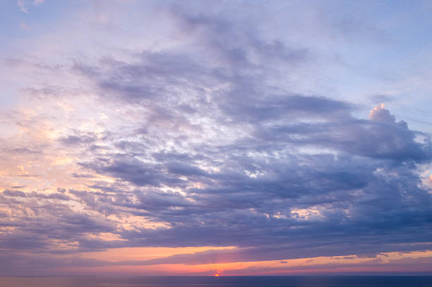 Wide layers of soft lavender and peach clouds stretch across the sky as the sun sets over the tranquil Mediterranean Sea. Gentle light and subtle color gradients create a peaceful, atmospheric mood.