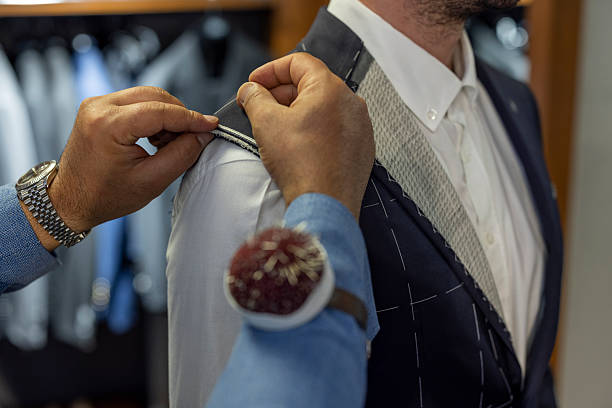 Professional tailor pinning a men’s suit jacket during a custom fitting session. Close-up view of hands adjusting fabric with pins, representing bespoke tailoring, precision craftsmanship, luxury menswear and high-end fashion service.