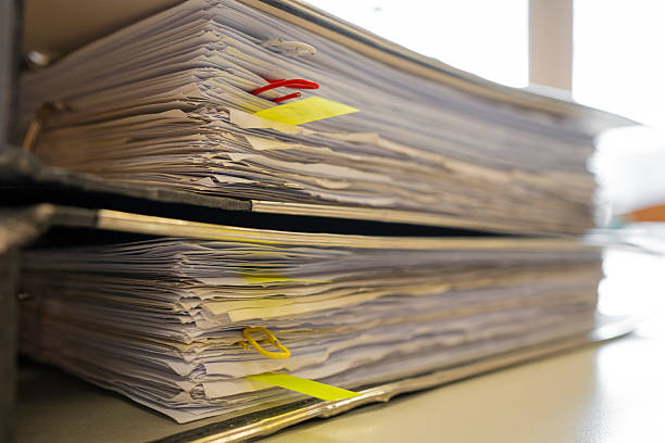 Stacks of old paper documents stored in worn file folders inside an abandoned office archive. The neglected workspace is filled with aging records, dust, and signs of decay, creating a nostalgic and historical atmosphere.