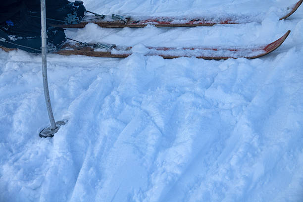 A close-up view of a skier's boots secured on green skis, set in a snowy mountain environment under a clear blue sky.