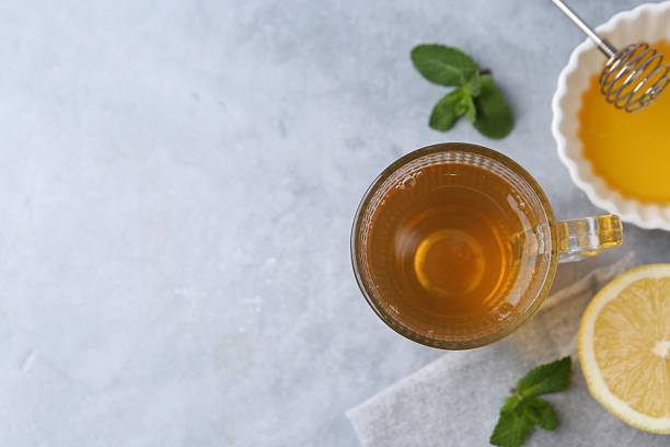 Aromatic mint tea in glass cup, fresh leaves, honey and lemon on light gray table, flat lay. Space for text