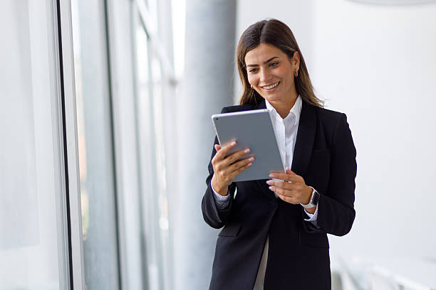 istock Businesswoman standing in modern office corridor, using digital tablet and smiling, connecting with technology 2255073308