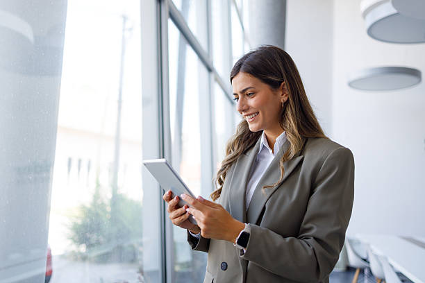 istock Businesswoman standing in modern office using digital tablet for work, smiling and communicating online 2255074878