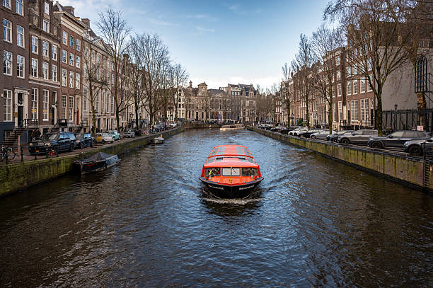 Amsterdam, Netherlands - January 3, 2026: Historic buildings and boats reflected in calm canal waters under a winter sky.