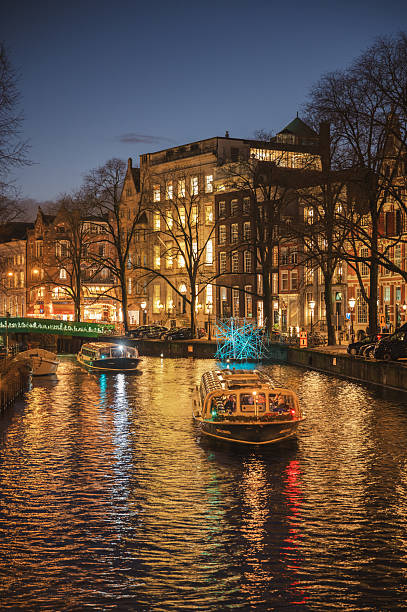Amsterdam, Netherlands - January 3, 2026: Historic buildings and boats reflected in calm canal waters under a winter sky.