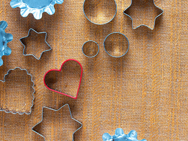 Various metal cookie cutters on a textured surface, including circles, stars, scalloped, and red heart shapes. Used for baking cookies, fondant, or play-dough
