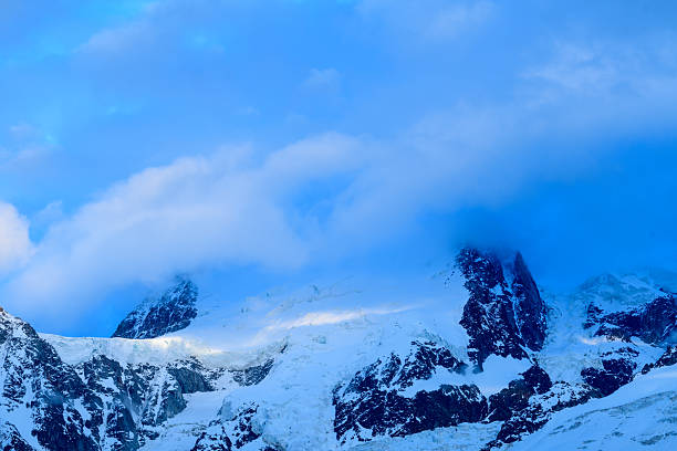 Soft blue clouds drift across the snowy peaks of Mont Blanc du Tacul, partially veiling the rugged mountain ridges and creating a serene, atmospheric alpine scene.