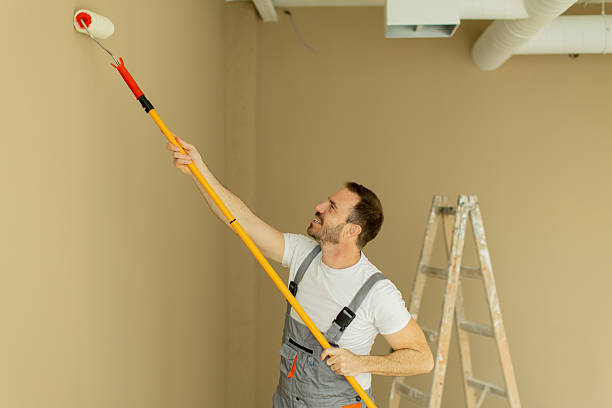 istock Man painting a wall with a roller while standing near a ladder in a light-colored room 2255087761