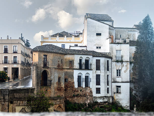 View of weathered white and stone buildings clinging to the edge of the dramatic gorge in Ronda, showcasing austere Andalusian architecture and the historic character of this iconic town in southern Spain.