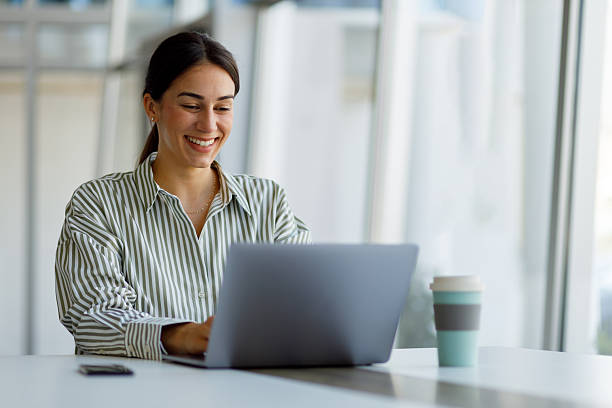 istock Young woman smiling and working with a laptop, enjoying her remote work. A reusable coffee cup is on the desk 2255091231